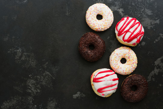 Various glazed donuts on a dark stone background. Top view, copy space.
