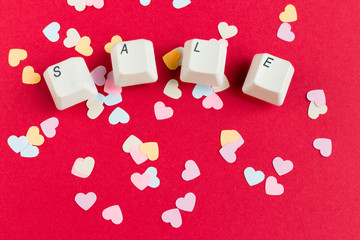 Computer keyboard keys with sale word written using the white buttons with paper heart shaped confetti on red background. Valentine's card. Discount concept.