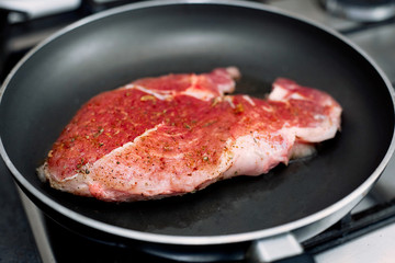 Raw pork chop in a frying pan with rosemary, pepper and salt.