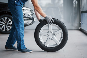 Mechanic holding a tire tire at the repair garage. replacement of winter and summer tires - obrazy, fototapety, plakaty