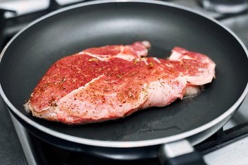 Raw pork chop in a frying pan with rosemary, pepper and salt.