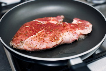 Raw pork chop in a frying pan with rosemary, pepper and salt.