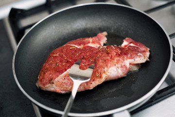 Raw pork chop in a frying pan with rosemary, pepper and salt.