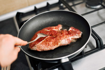 Raw pork chop in a frying pan with rosemary, pepper and salt.