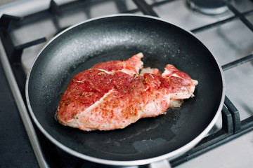 Raw pork chop in a frying pan with rosemary, pepper and salt.