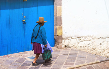 Peruvian elderly woman in traditional dress on the street of Cusco, Peru, Latin America. horizontal, brown hat, blue door, selective focus