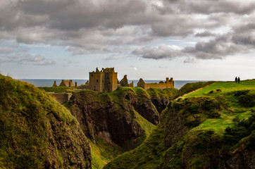 Fototapeta premium A couple enjoying romantic and dramatic ruins of medieval fortress Dunnottar castle on rocky cliffs of North Sea coast in Stonehaven, Aberdeen, Scotland