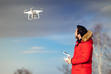 Portrait of man with red winter jacket flying drone, operating uav hobby aircraft. Man piloting...