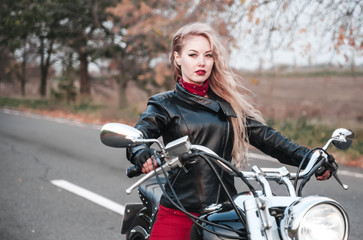 A stylish biker woman posing outdoor with motorcycle. 
