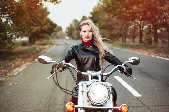 A stylish biker woman posing outdoor with motorcycle. 
