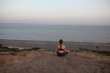 Unrecognizable young woman Practicing Yoga in Lotus pose sitting on the edge of rock against of see. Padmasana