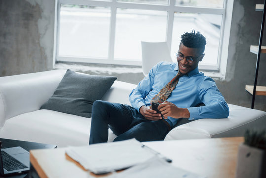 Close up. Smiling afroamerican guy sitting on the couch and looking at his smartphone
