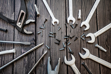 A set of tools on a wooden background: screwdrivers, pliers, adjustable wrench, open-end wrench, screws, dowel.