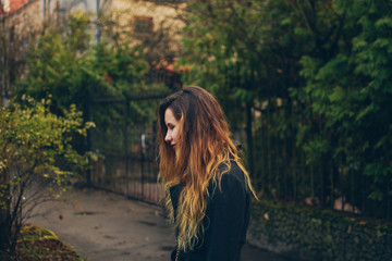 Profile of a handsome young caucasian girl in standing on the sidewalk. Beautiful long-haired girl looking down. High contrast, sharp clarity, and green background.