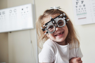 Happy childhood. Focused portrait of little girl in phoropter looking straight into the camera and...
