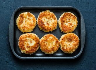 Potato bread crumbs baked cakes on a baking tray on a dark background, top view