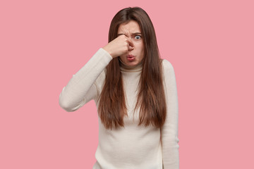 Ugh, what disgusting smell. Discontent brunette woman covers nose, feels bad reek, wears casual...