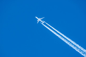 An airplane and a trail from an airplane in a blue sky - obrazy, fototapety, plakaty