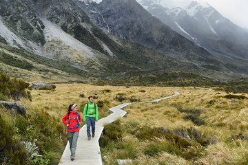 New Zealand trampers backpacking on Mount Cook / Aoraki Hooker valley travel. hikers hiking walking on Hooker Valley Track in summer on boardwalk. Couple on travel holiday adventure.