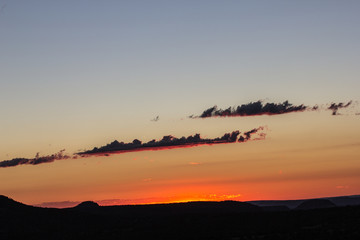 Sunrise silhouettes the trees, the mountains, and the clouds.  