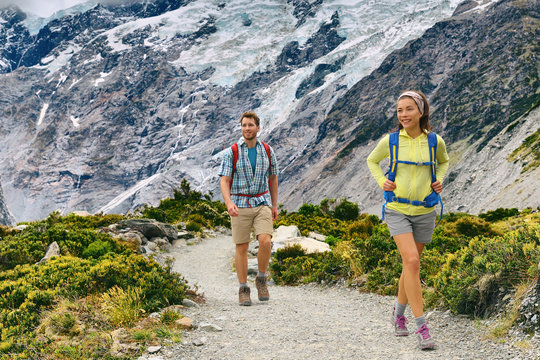 New Zealand tourists people tramping with backpacks on Mount Cook / Aoraki Hooker valley travel. Backpacking hikers hiking on Hooker Valley Track. Couple walking.