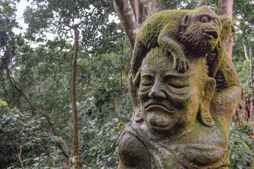 Fototapeta na wymiar Statue of a monkey sitting on a human head covered by moss in the Sacret Monkey Forest in Ubud Bali Indonesia