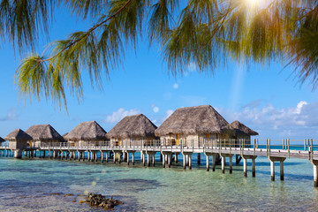 authentic houses with a straw roof over water of the blue sea and the sky with clouds. Polynesia...