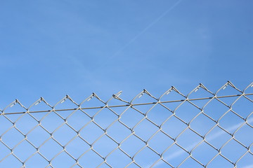 A close up photograph of a section of wire fencing, against a blue sky.  Security, safety concept. Barrier