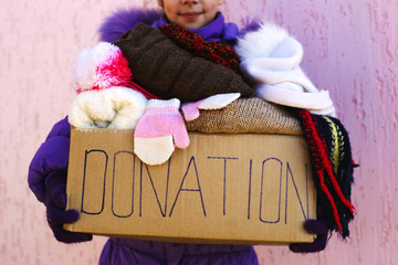Girl holding donation box with warm winter clothes.
