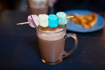 Hot chocolate drink with colored marshmallows and pie on the background 