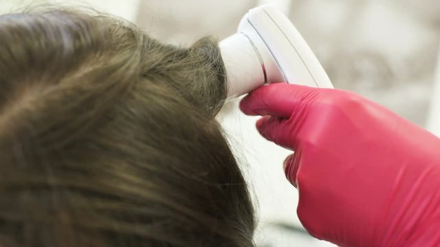 doctor dermatologist diagnoses the structure of the hair of a young pretty girl with a special tool - a trichoscope. Trichology, trichogram