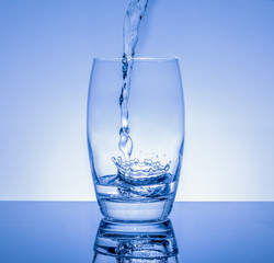 Frisches Getränk in das Glas giessen - Wasser spritzt im Glas auf blauem Hintergrund