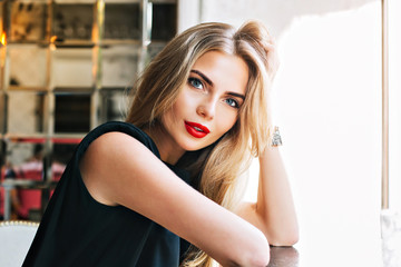 Closeup portrait beautiful woman leaning on table in cafeteria. She has red lips, long blonde hair,...