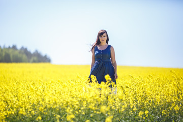 Girl in a blue dress leaves in a field of rapeseed. Follow me concept