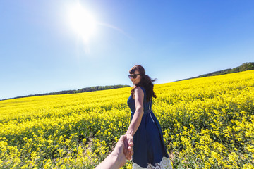 Fototapeta premium Girl in a blue dress leaves in a field of rapeseed. Follow me concept