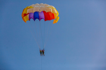 Spectacular scenic view on the sea and blue sky with people flying on a colorful parachute towed by a motor boat