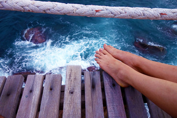 Female Feet on a wooden platform above sea and rocks