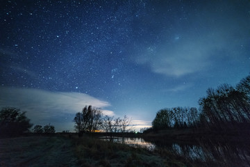 Abandoned old cars, against the background of the night sky with millions of stars around, near the picturesque lake.