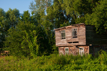 Light blue sky in the warm summer over the old abondoned house built from wood far away in the forest. Green trees near. Travelling on the suburb roads 