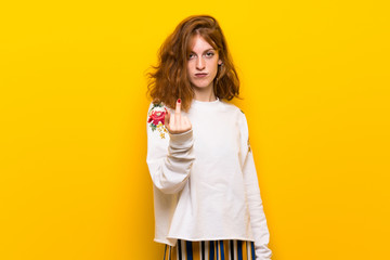 Young redhead woman over yellow wall making horn gesture