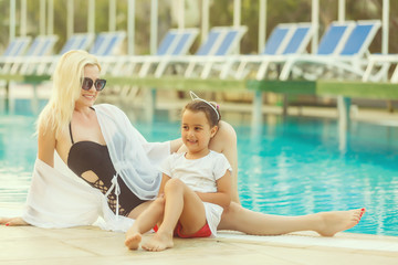 portrait of smiling beautiful woman and her little cute daughter in sunglasses near pool outdoor