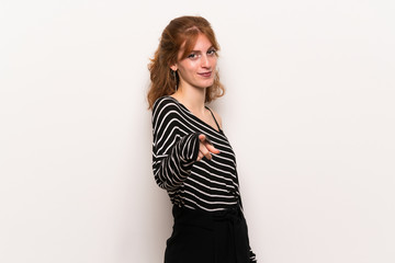 Young redhead woman over white wall points finger at you with a confident expression