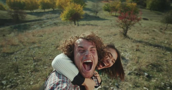 A beautiful multicultural cuple spending a nice time together in the middle of mountain, taking a selfie video and playing funny in front of a camera.