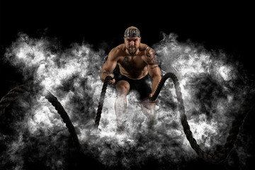 Men working out with battle ropes. Dark smoke background