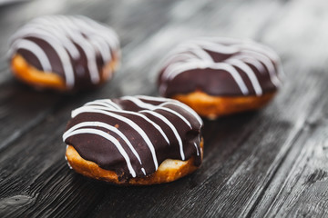Donuts with chocolate glaze with stripes, on wooden table blurry background.