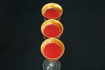 Golden glasses filled with a red liquid in black background