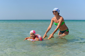 A young mother with a little daughter swim in the sea on a hot summer day.