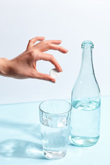 Female hand throws a pill into a glass of water. Minimalistic concept.