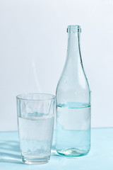 A glass bottle with clear water and a glass on a white-blue background. Minimalistic creative concept.