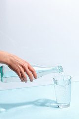 Female hand pours pure mineral water from a bottle into a glass. Minimalist design. The concept of healthy eating.